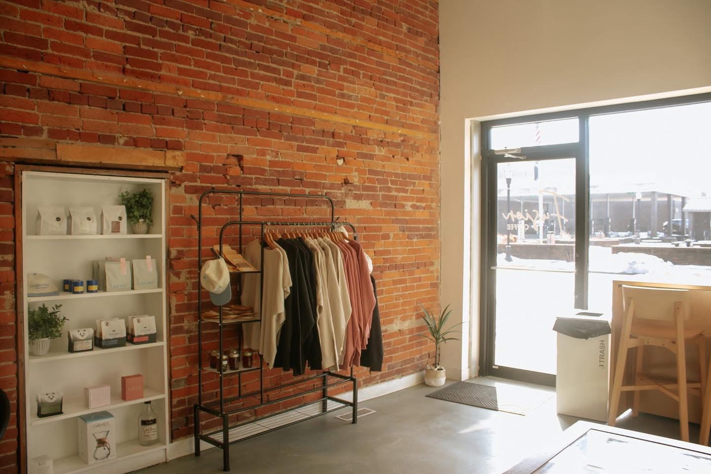 Branded coffee bags and apparel on a rack against brick.